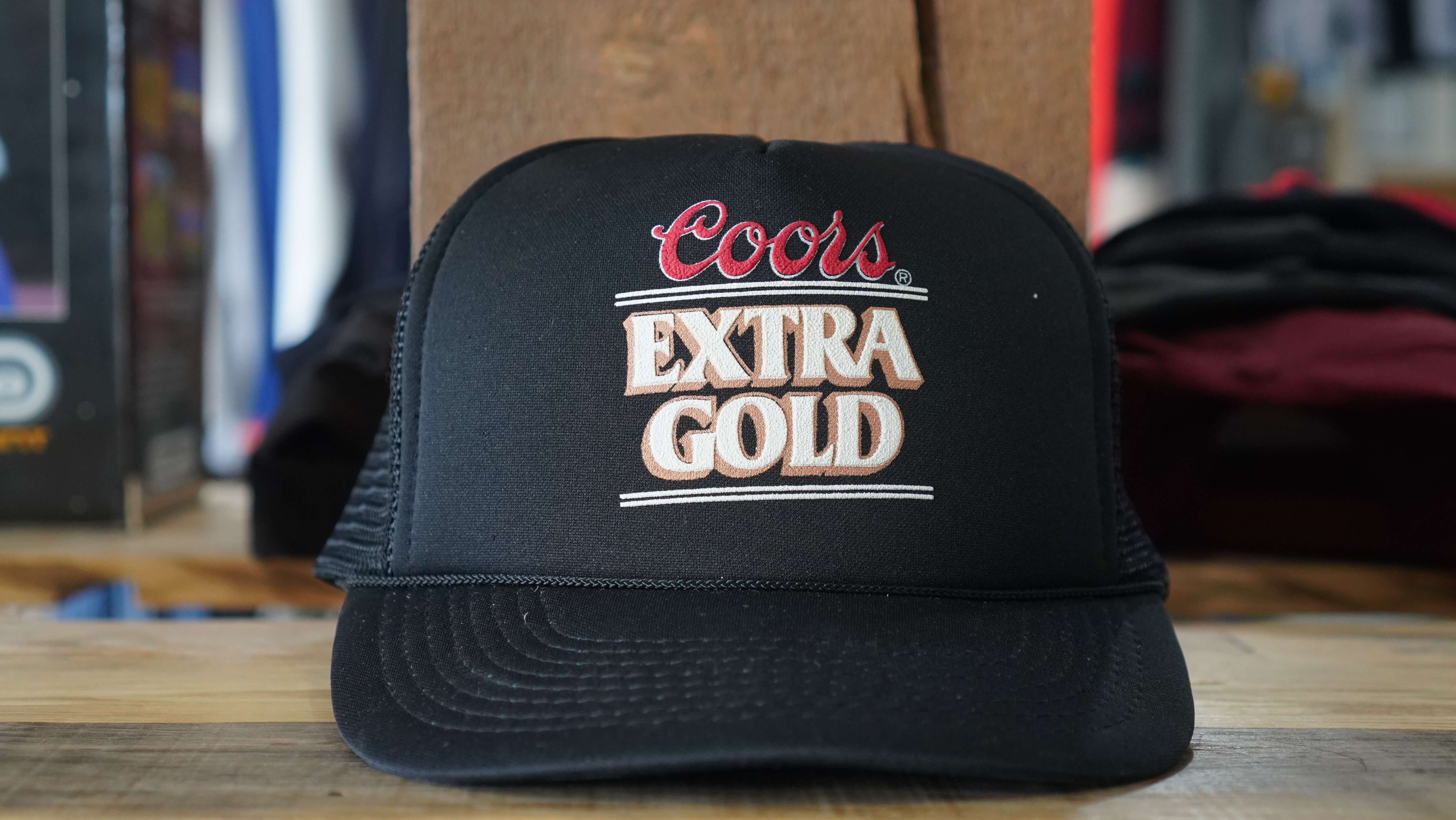 90s Coors Extra Gold vintage black trucker hat with red and gold logo, from West Block Vintage, capturing the essence of 90s brewery advertising and trucker style.